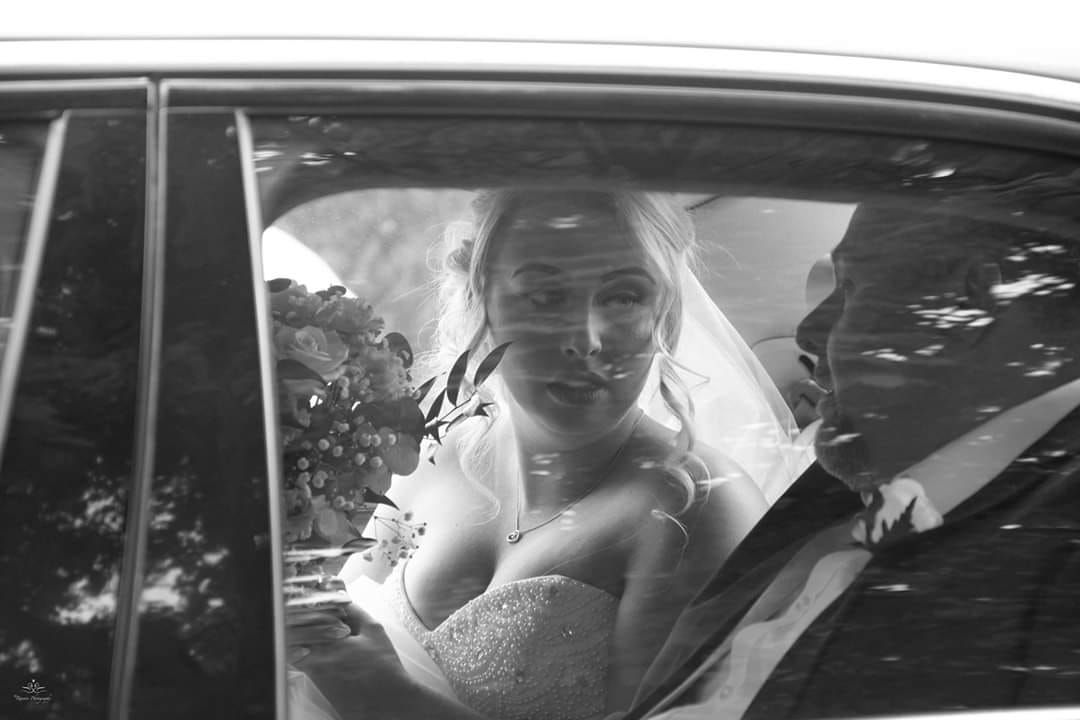 A candid black and white photo of a bride smiling through a car window on her wedding day.
