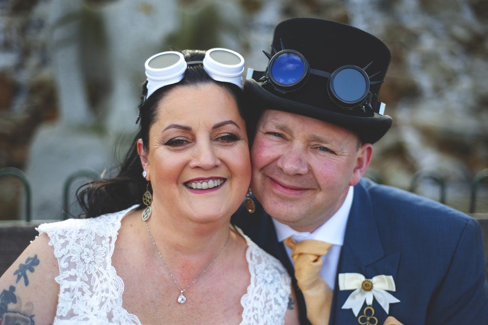 A festive couple pose together at their steampunk-themed wedding with unique accessories and attire.