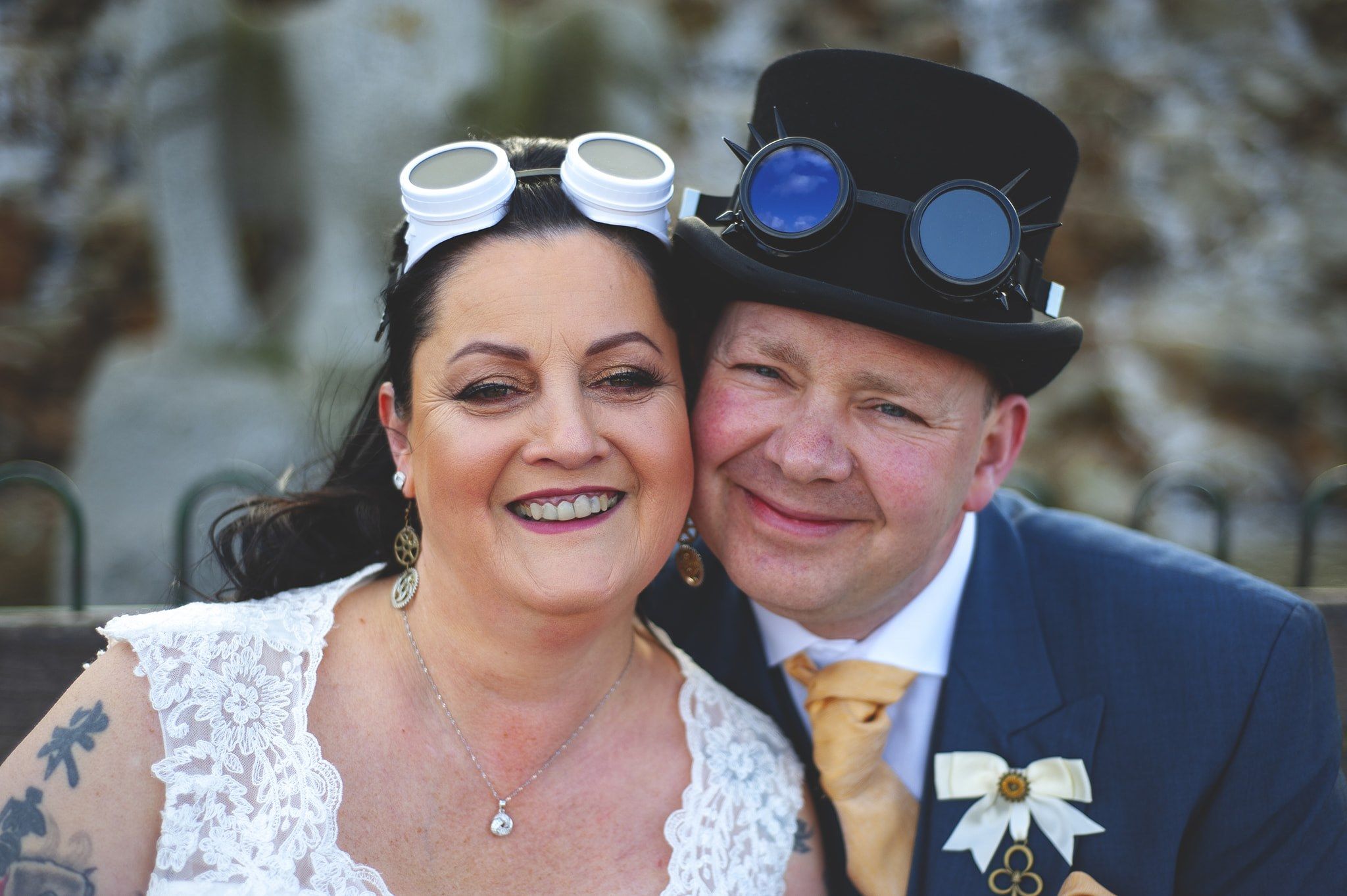 A festive couple pose together at their steampunk-themed wedding with unique accessories and attire.