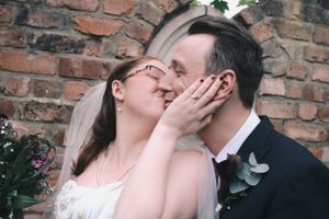 Intimate wedding moment captured against rustic brick wall backdrop.