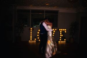 Silhouetted couple dancing in dark room with illuminated LOVE sign in background.