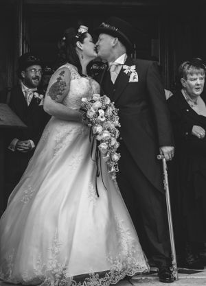 Black and white wedding photo capturing couple's kiss surrounded by guests.