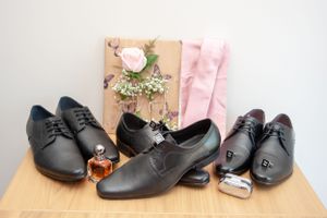 Collection of formal black dress shoes arranged with pink gift boxes and floral decorations.