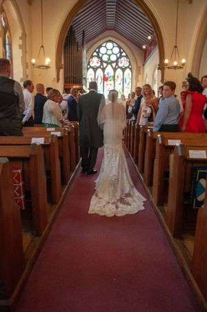 Traditional church wedding ceremony with stained glass window and guests in pews.