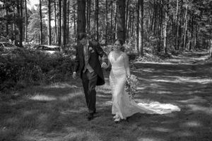 Black and white photo of newlyweds walking together along a forest path.