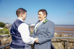A couple holds hands on a seaside balcony on a bright sunny day.
