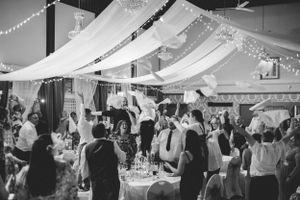 A black and white shot of wedding reception guests celebrating under decorative draped fabric.
