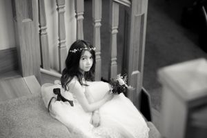 A bride in a white gown sits gracefully on stairs wearing a delicate floral crown.
