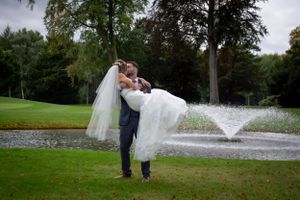 A groom lifts his bride dramatically by a fountain in a romantic outdoor setting.