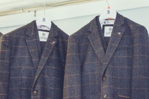 Two matching tweed suits hanging on display.