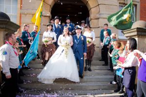 Wedding couple exits venue while guests wave colorful flags and throw confetti on the steps.
