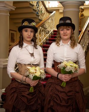 Two attendants in steampunk-inspired outfits with corsets and top hats holding bouquets.