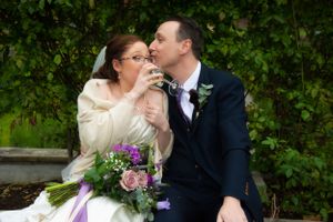 Romantic moment shared between couple with purple bouquet against green foliage.