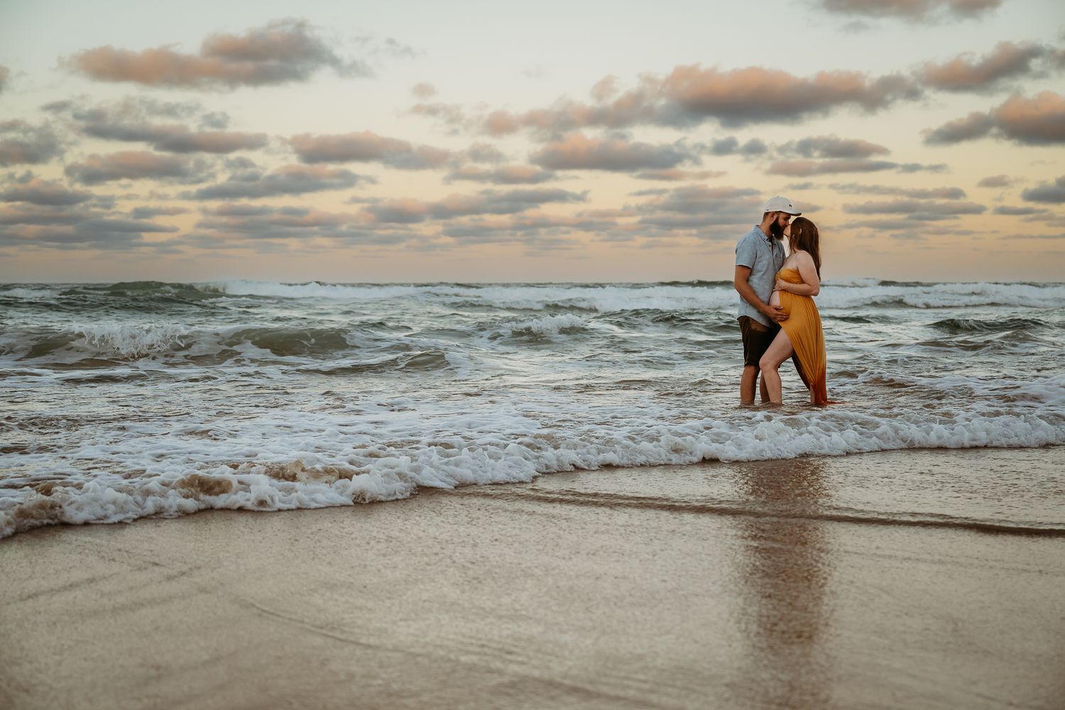 A romantic beach scene with crashing waves and sunset clouds in the background.