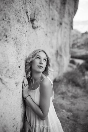 Portrait against a textured rock wall showing a dreamy expression in black and white.