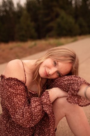 A dreamy portrait in a brown floral dress sitting on the ground during golden hour.