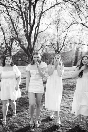 Group wearing white dresses laughing together in a park setting.