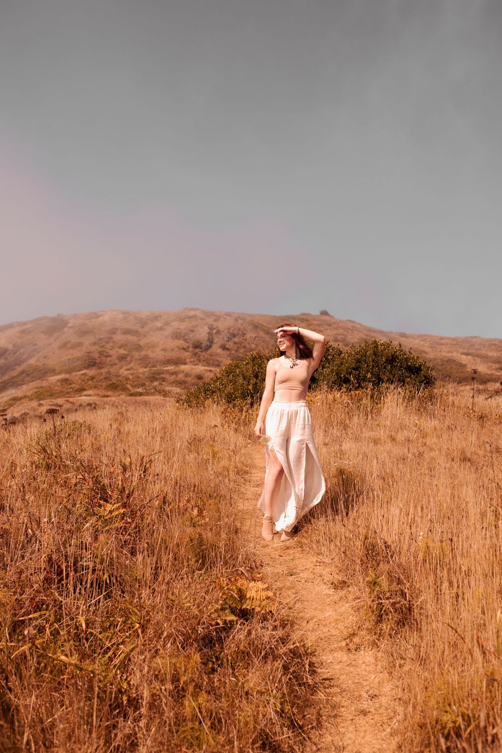 White dress flowing in wind along coastal hiking trail at sunset.