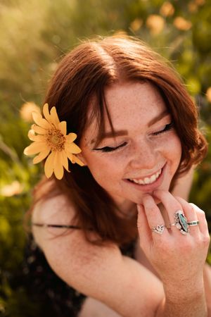 Candid smiling portrait with yellow flower and statement rings in golden light.