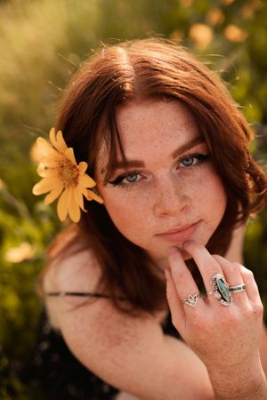Portrait with a yellow daisy flower in hair and vintage rings in warm sunlight.