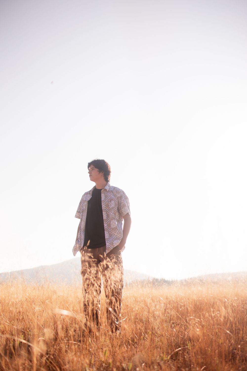 A person standing in tall golden grass wearing casual clothing at sunset.