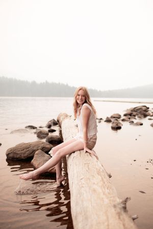 A peaceful lakeside scene with a driftwood log and rocky beach at sunset.
