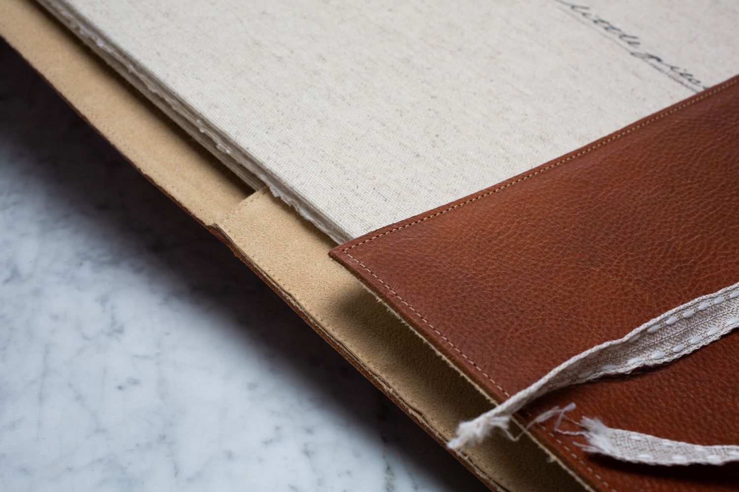 Close-up detail of a brown leather notebook binding with white pages showing craftsmanship and texture.