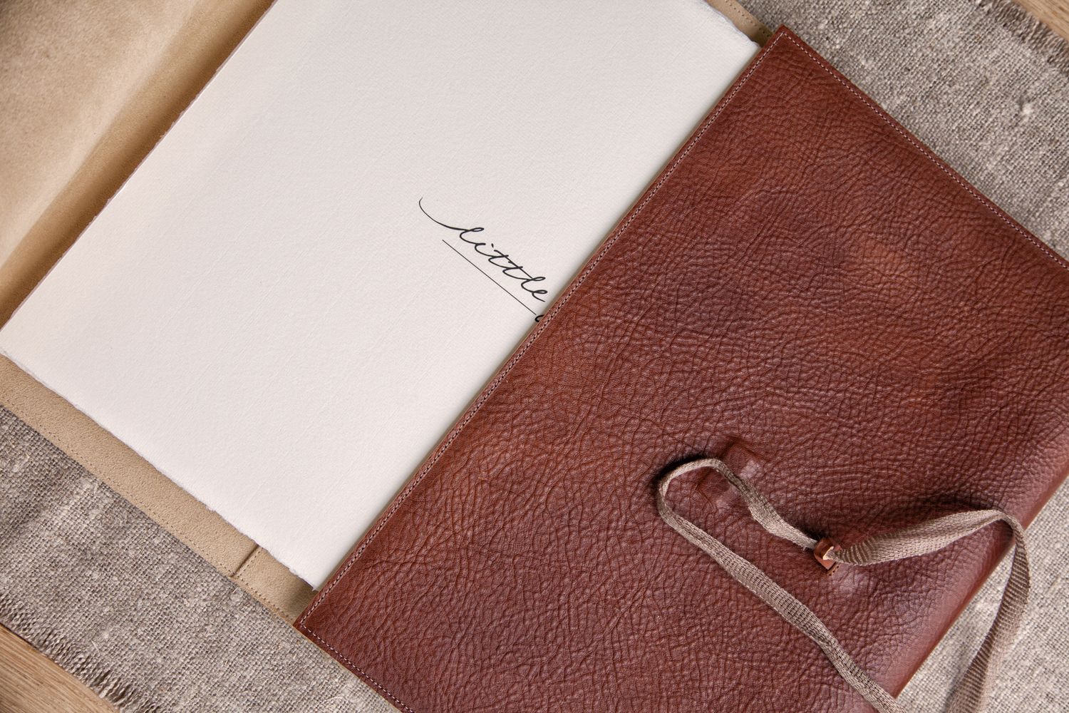 Overhead view of an open leather journal with handwritten text and leather tie closure.