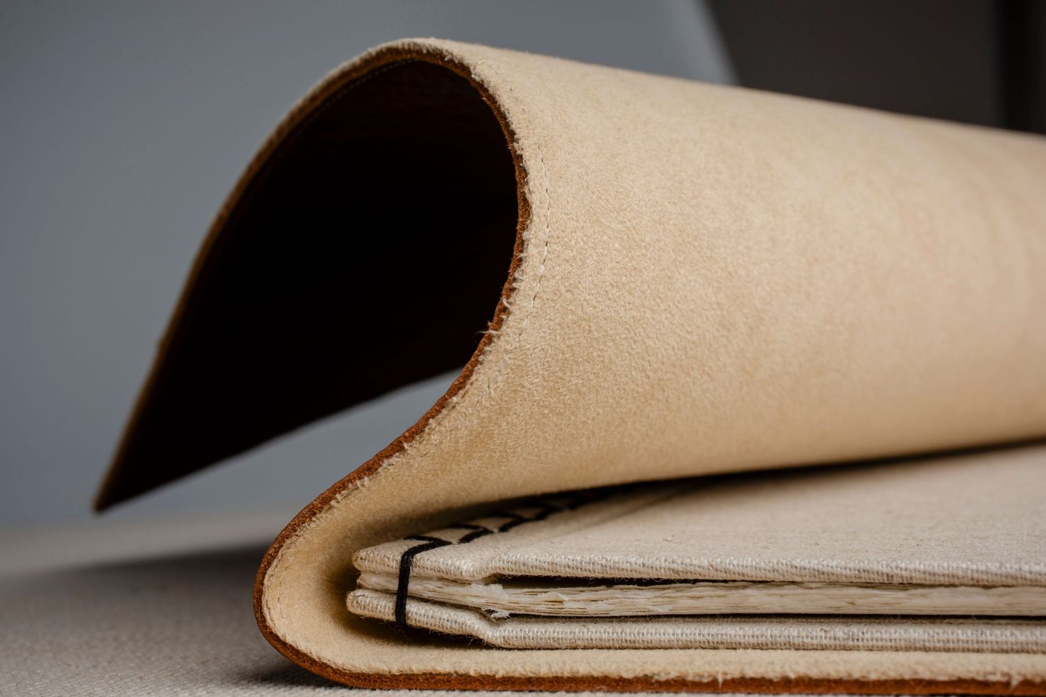 Artistic curved detail of tan leather and paper book binding against dark background.