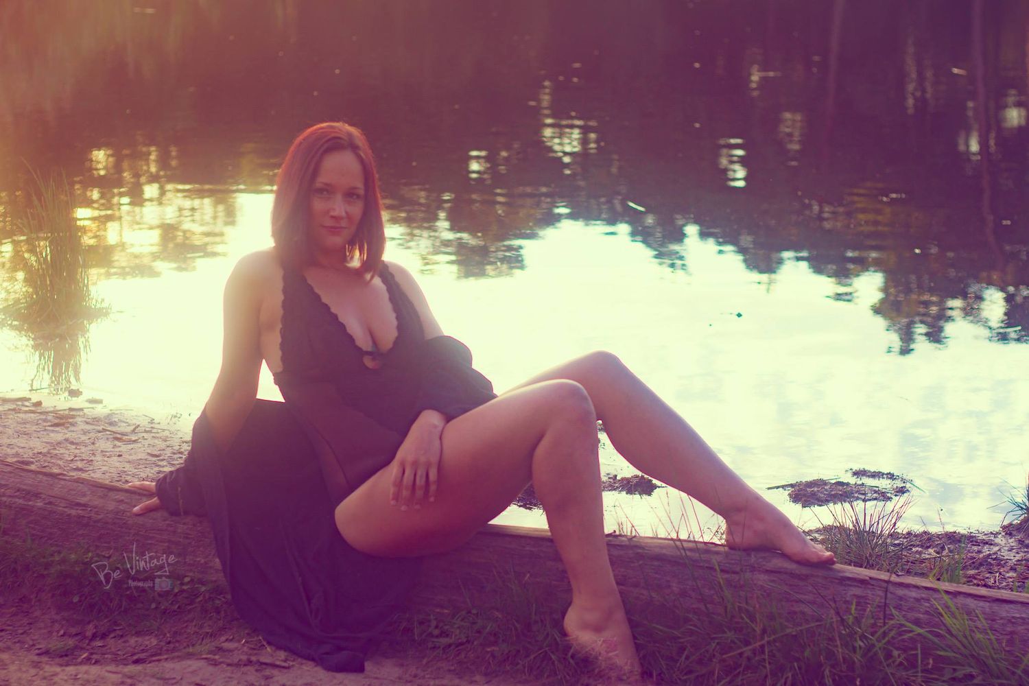 Stylish boudoir portrait of a woman relaxing by a reflective lake during golden hour.