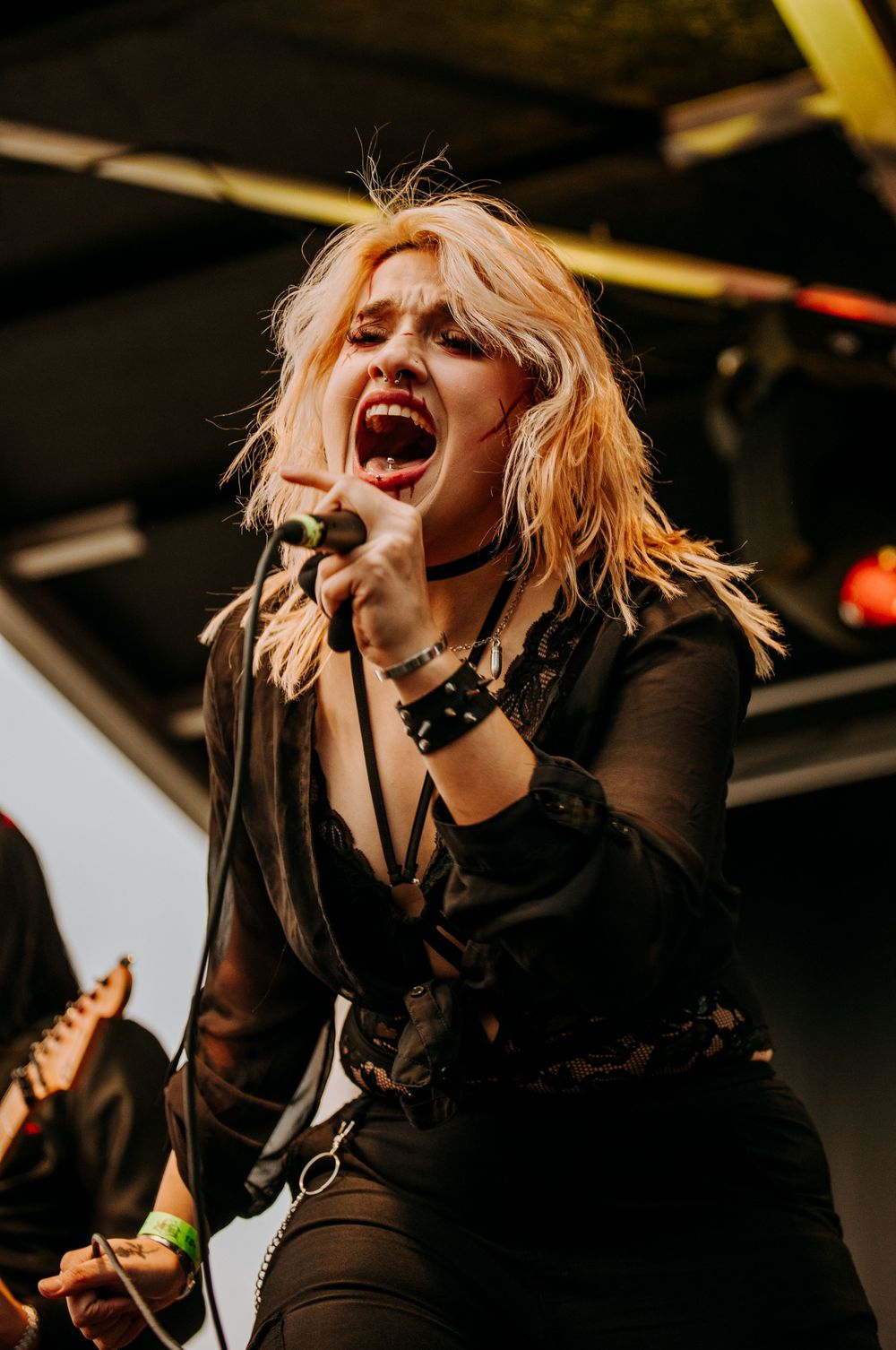A performer in black attire sings emotionally into a microphone during a concert.