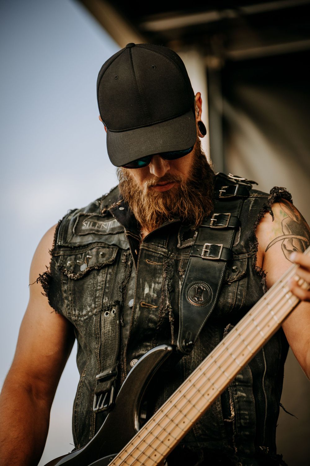 A bassist in a leather vest and baseball cap plays during a live performance.