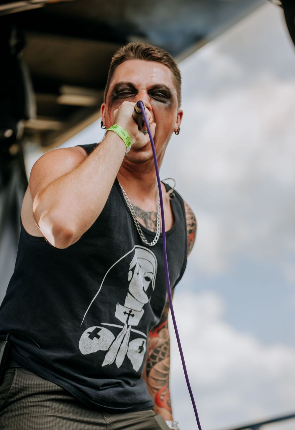 Metal vocalist in black tank top sings intensely during outdoor festival performance.