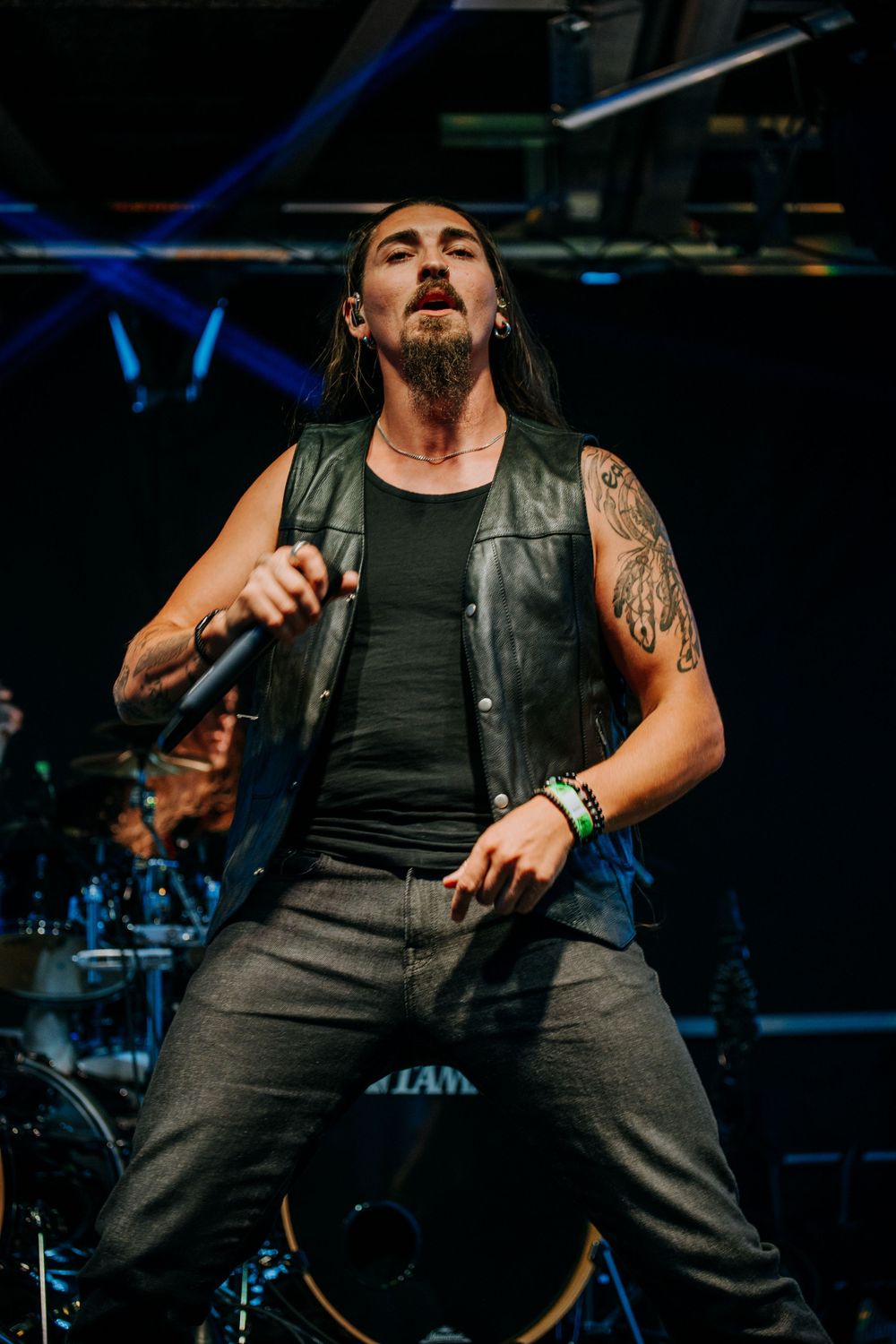 A performer in a leather vest strikes a dramatic pose during a concert performance.