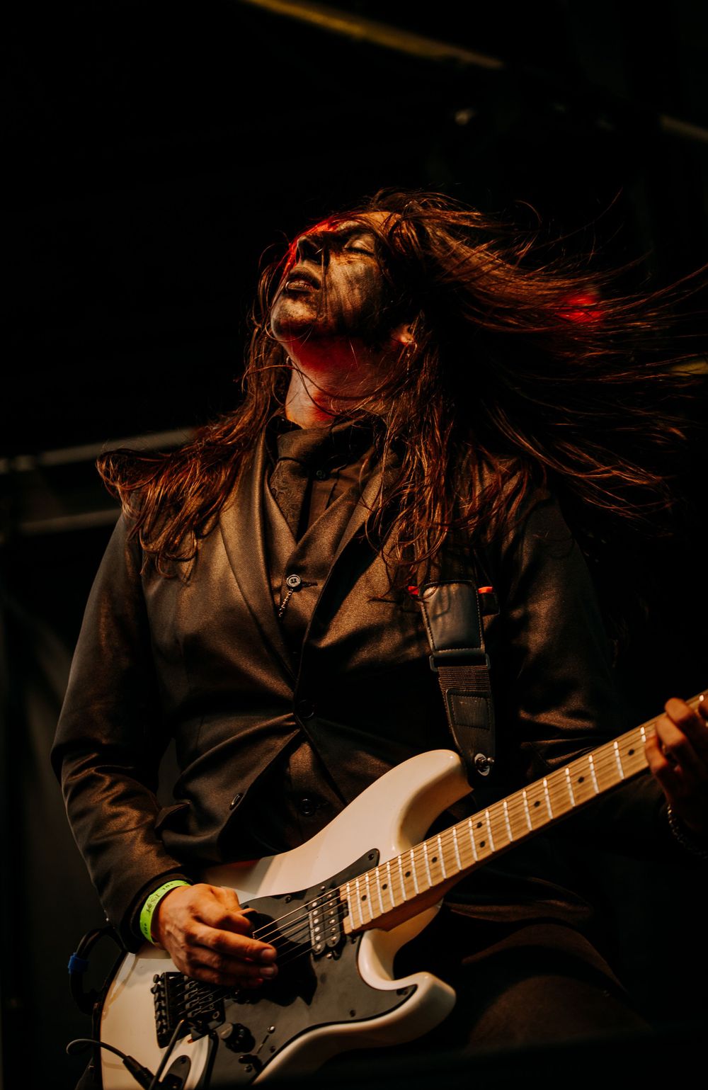 A guitarist with long flowing hair performs passionately on stage with dramatic lighting.