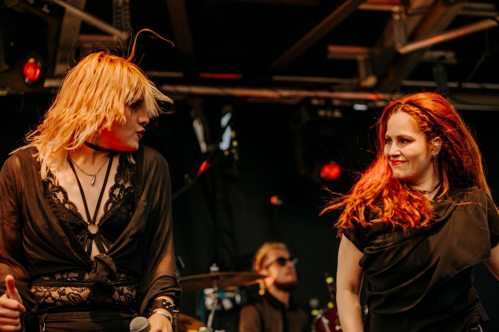 Two performers with contrasting hair colors interact on stage during a rock show.