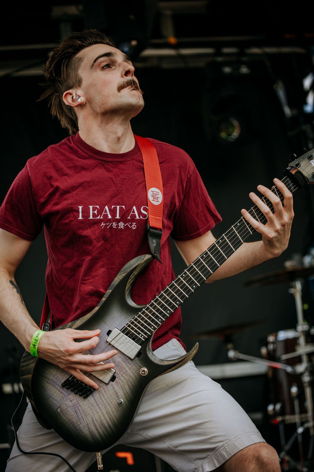 Guitarist in red TEATAS shirt plays modern electric guitar during outdoor performance.