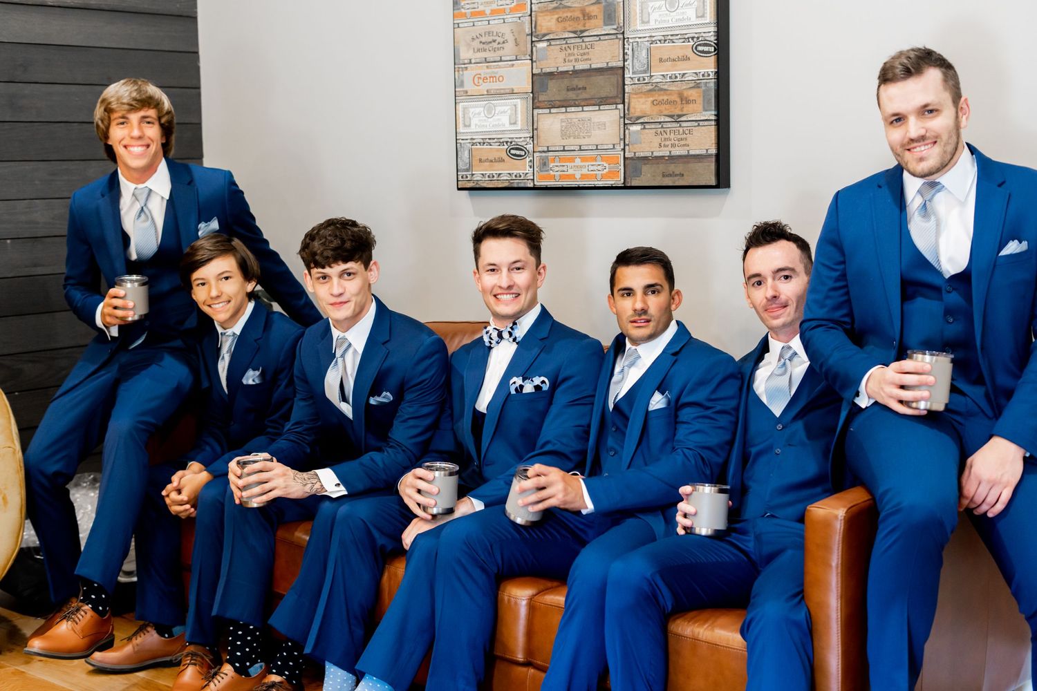Groomsmen in matching navy suits relax on leather chairs before ceremony.