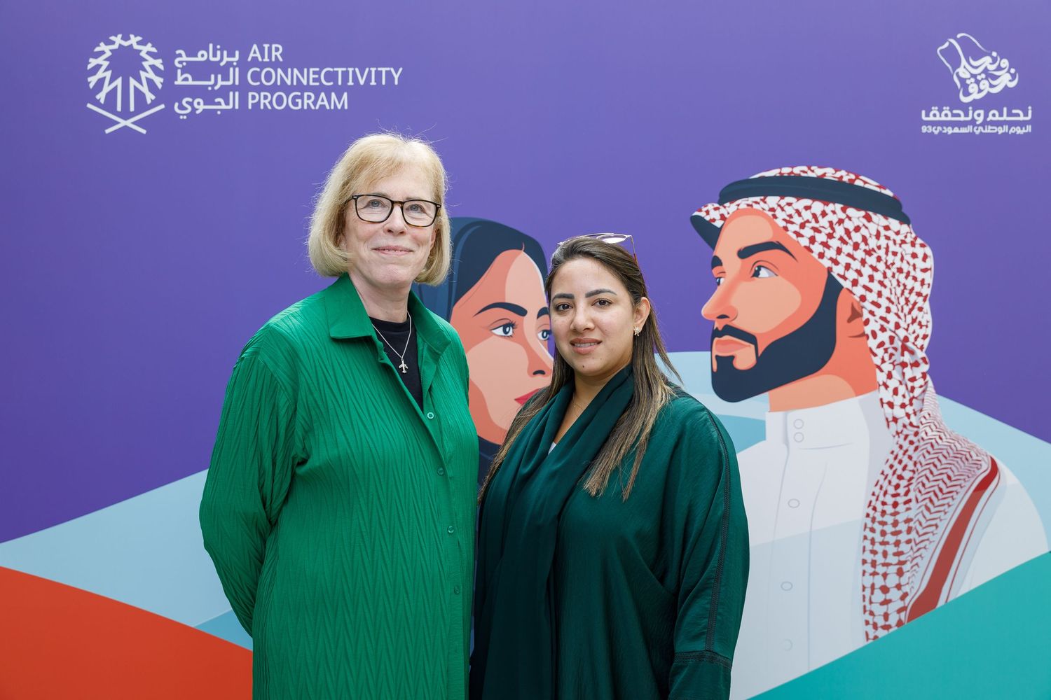 People posing in front of a branded wall with traditional Middle Eastern artwork.