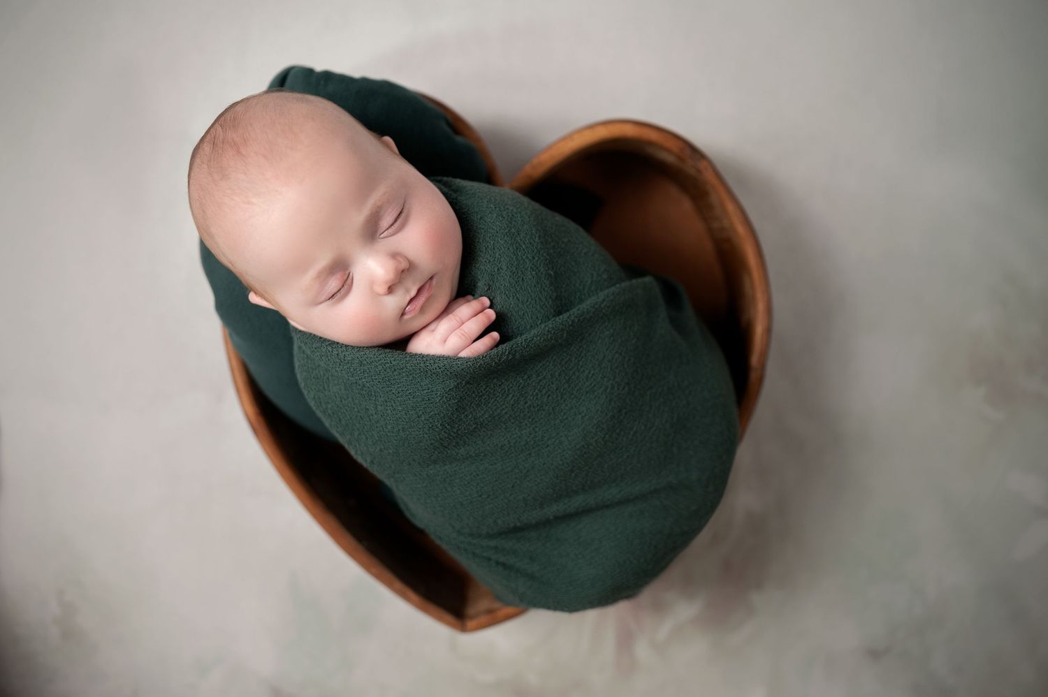 Artistic newborn photography series with baby wrapped in dark fabric against neutral background.