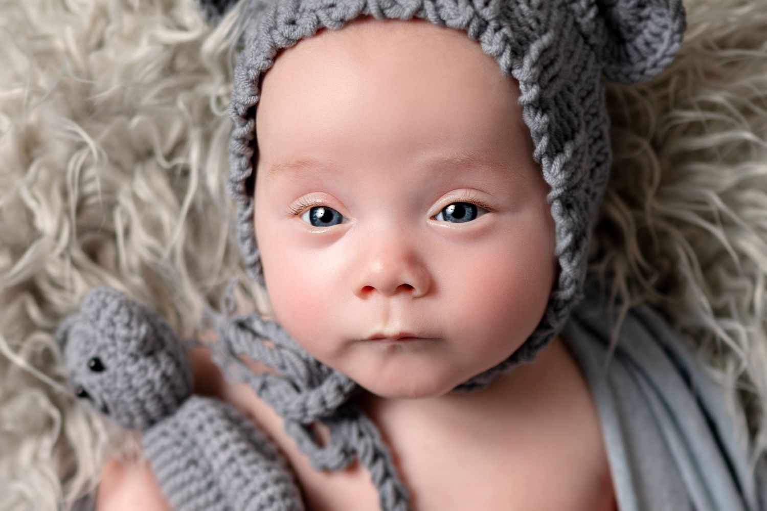Professional newborn portraits featuring grey knit accessories and fluffy textures.
