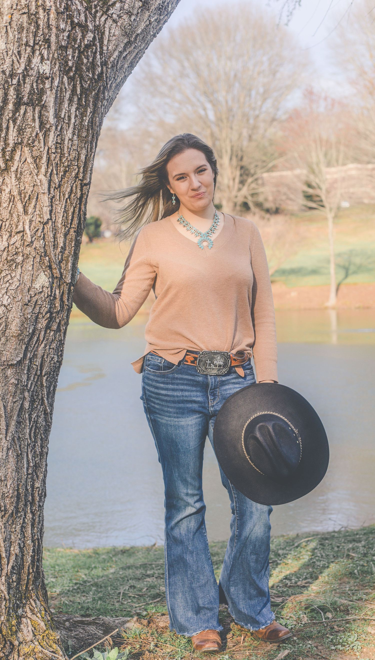 Casual outdoor portrait session by tree featuring western-style outfit with cowboy hat and jeans.