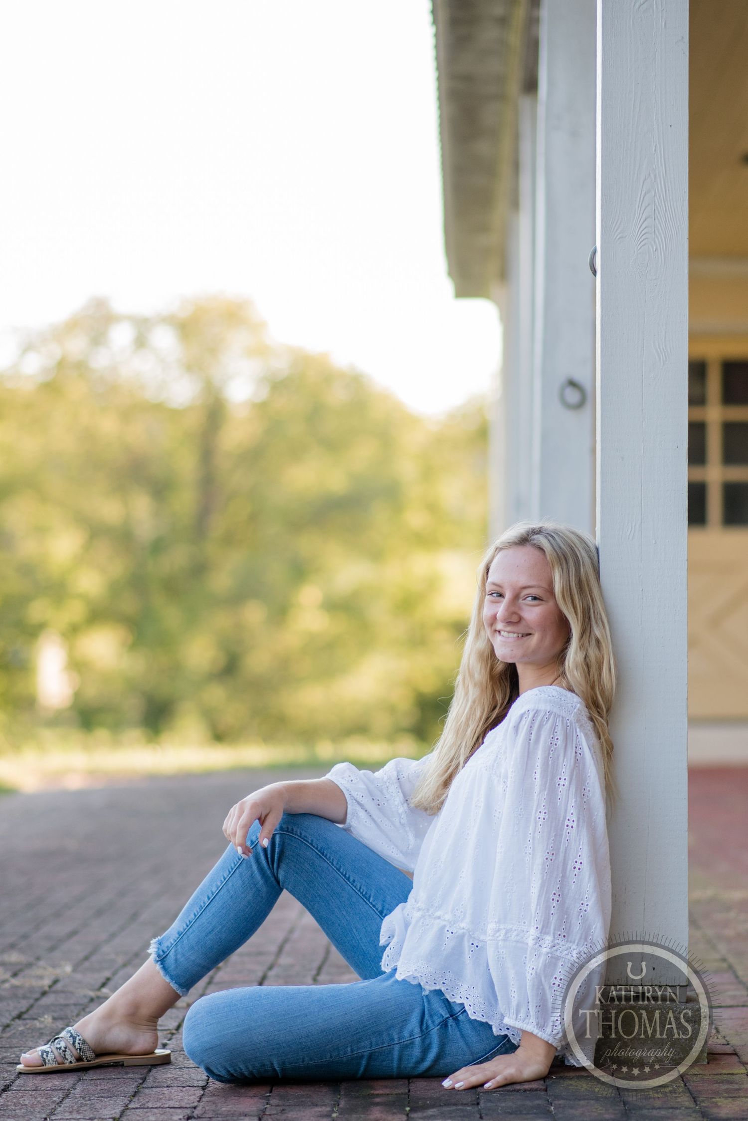 Casual outdoor portrait against a yellow building with flowing white top and fitted jeans.