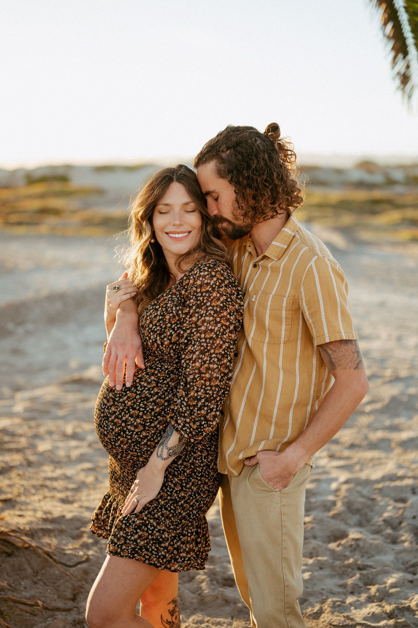 Coronado Beach sunset maternity photoshoot by Ventura maternity photographer of couple cuddling by palm tree