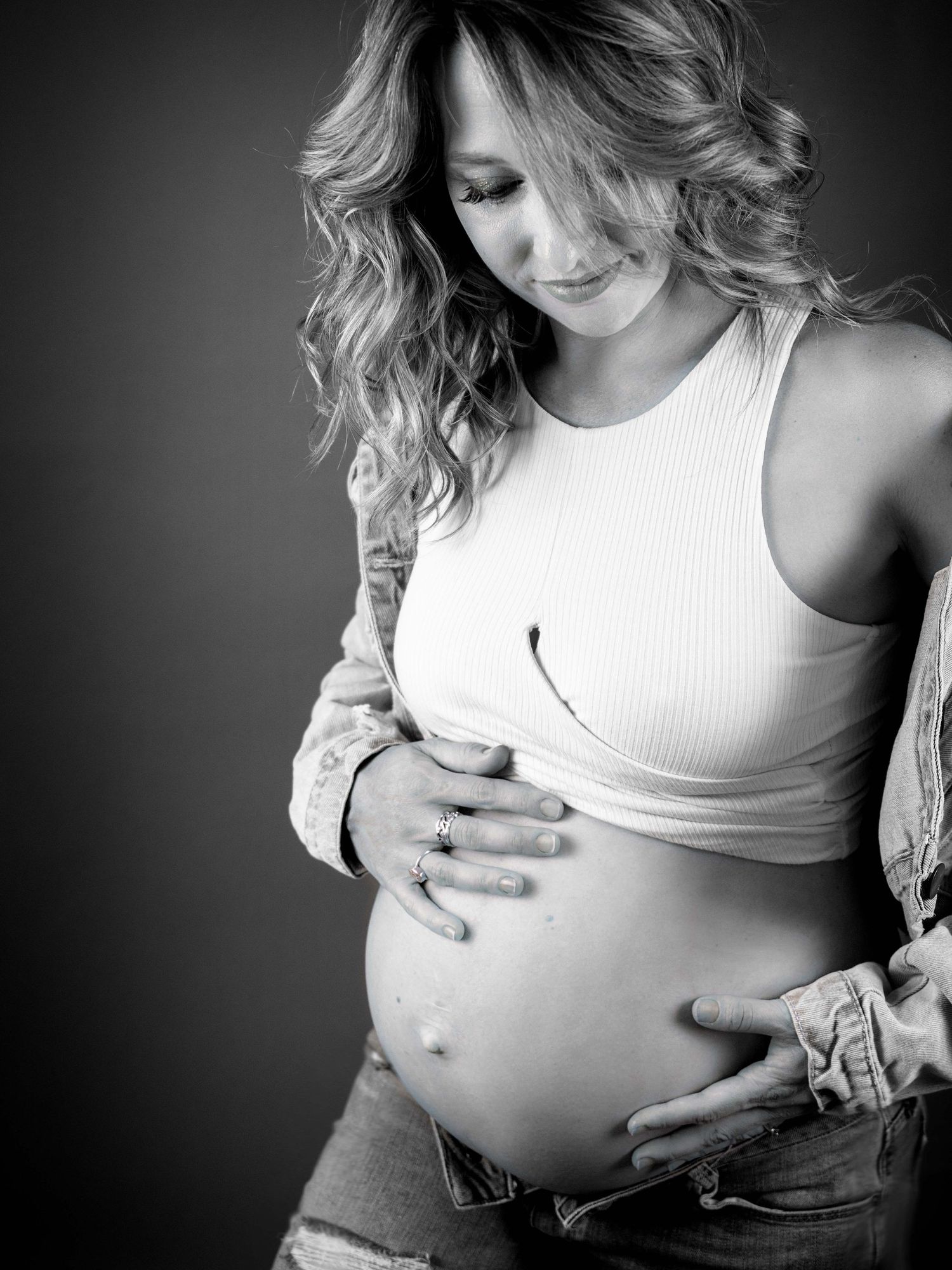 Maternity photoshoot female wearing demiun jeans and white top holding her 32 wk gestation pregnant belly