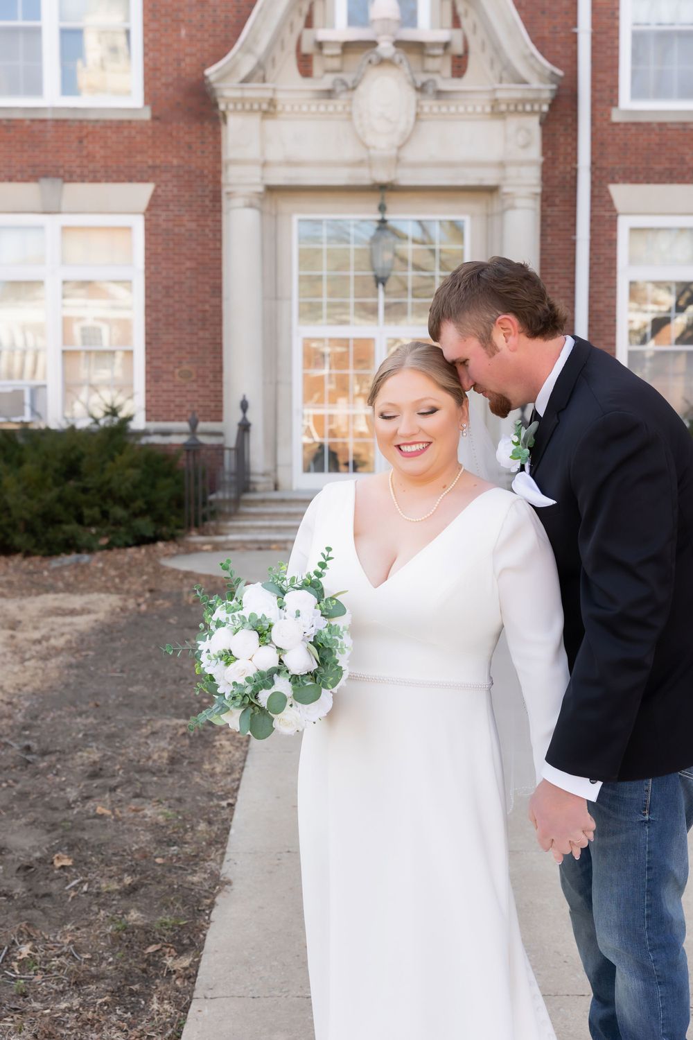 A winter wedding portrait outside a historic brick building with white floral bouquet.
