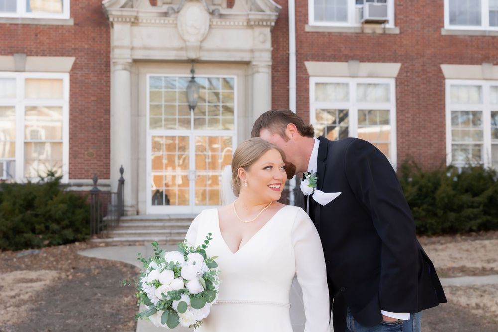 A wedding couple poses outside a classic brick building with ornate architectural details.
