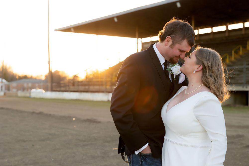 A tender moment between newlyweds backlit by golden sunset light at an outdoor venue.