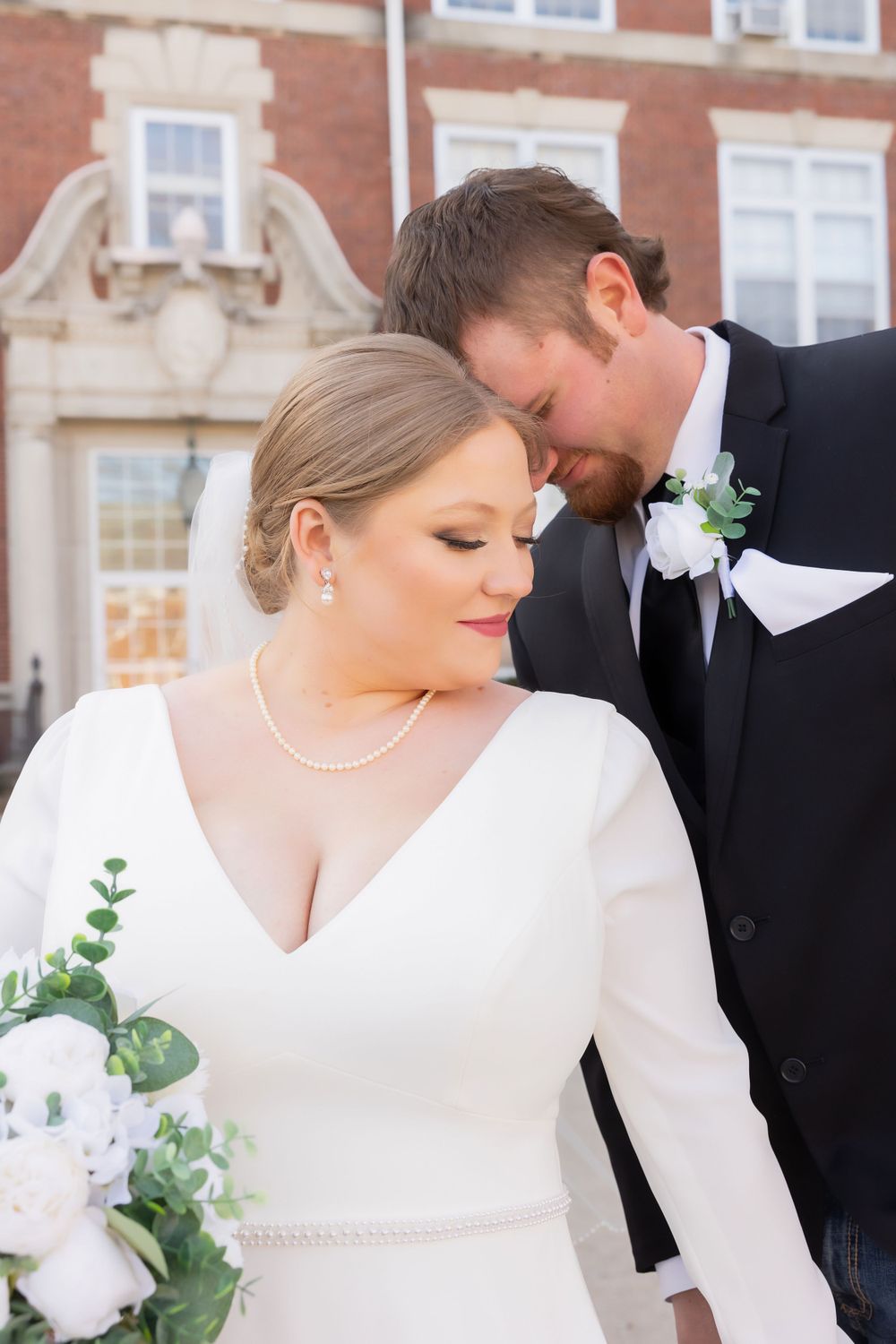 A tender wedding moment captured in front of a classic brick building with ornate detailing.