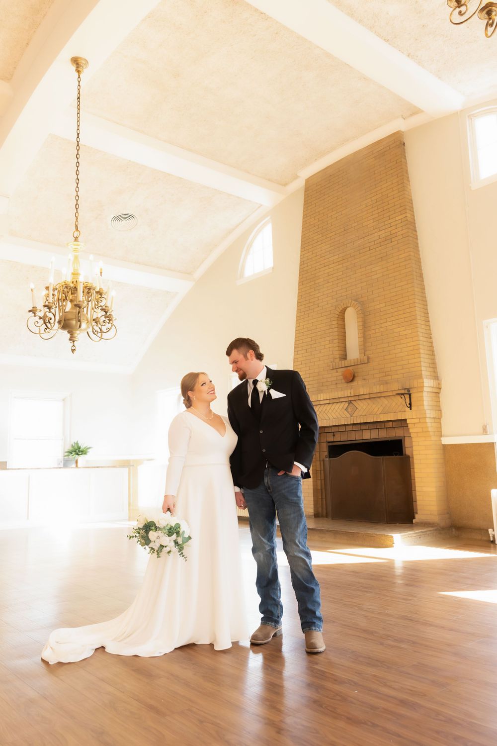 A wedding couple stands in a bright room with vaulted ceilings and a decorative brick fireplace.